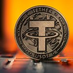 Tether USDT Cryptocurrency physical coin placed on laptop keyboard and lit with orange light from behind.
